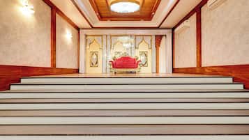 Una imponente escalera conduce a una habitación con una butaca tapizada de rojo y decoración ornamentada.