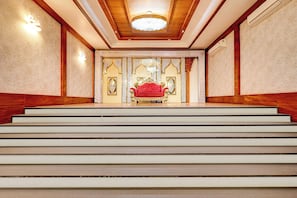 Una imponente escalera conduce a una habitación con una butaca tapizada de rojo y decoración ornamentada.