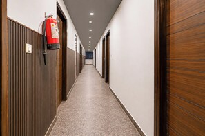 A corridor with wooden paneling on the walls, a fire extinguisher mounted on the left wall, and a tiled floor. - Townhouse Ranipur Mor Formerly Parmila (Haridwar)
