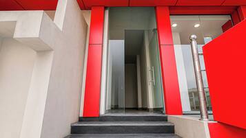 Una escalera conduce a una entrada con puerta de vidrio, una pared de acento roja y baranda metálica.