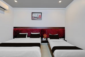 Quarto de hotel com duas camas, cabeceira vermelha, quadro na parede e mesa de cabeceira com um vaso de flores.