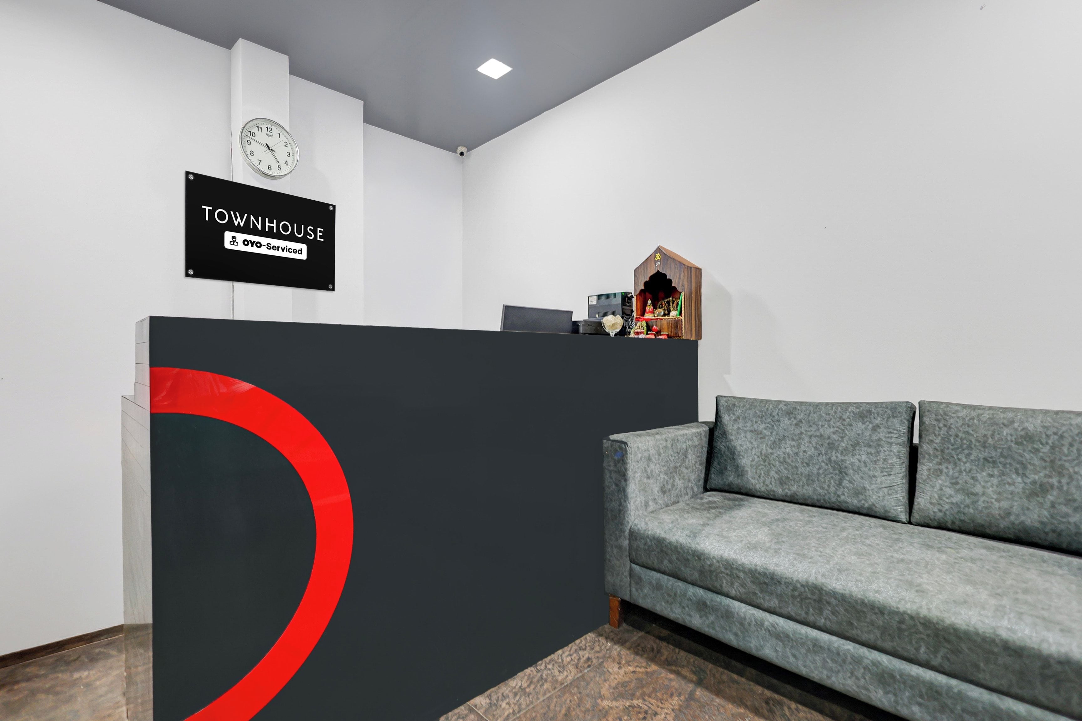 Una zona de recepción con un mostrador negro, un reloj y un pequeño santuario en la pared.