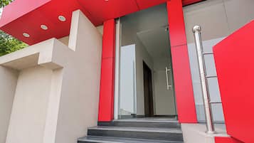 A modern building with a red facade, a glass entrance, and a metal handrail on the stairs.