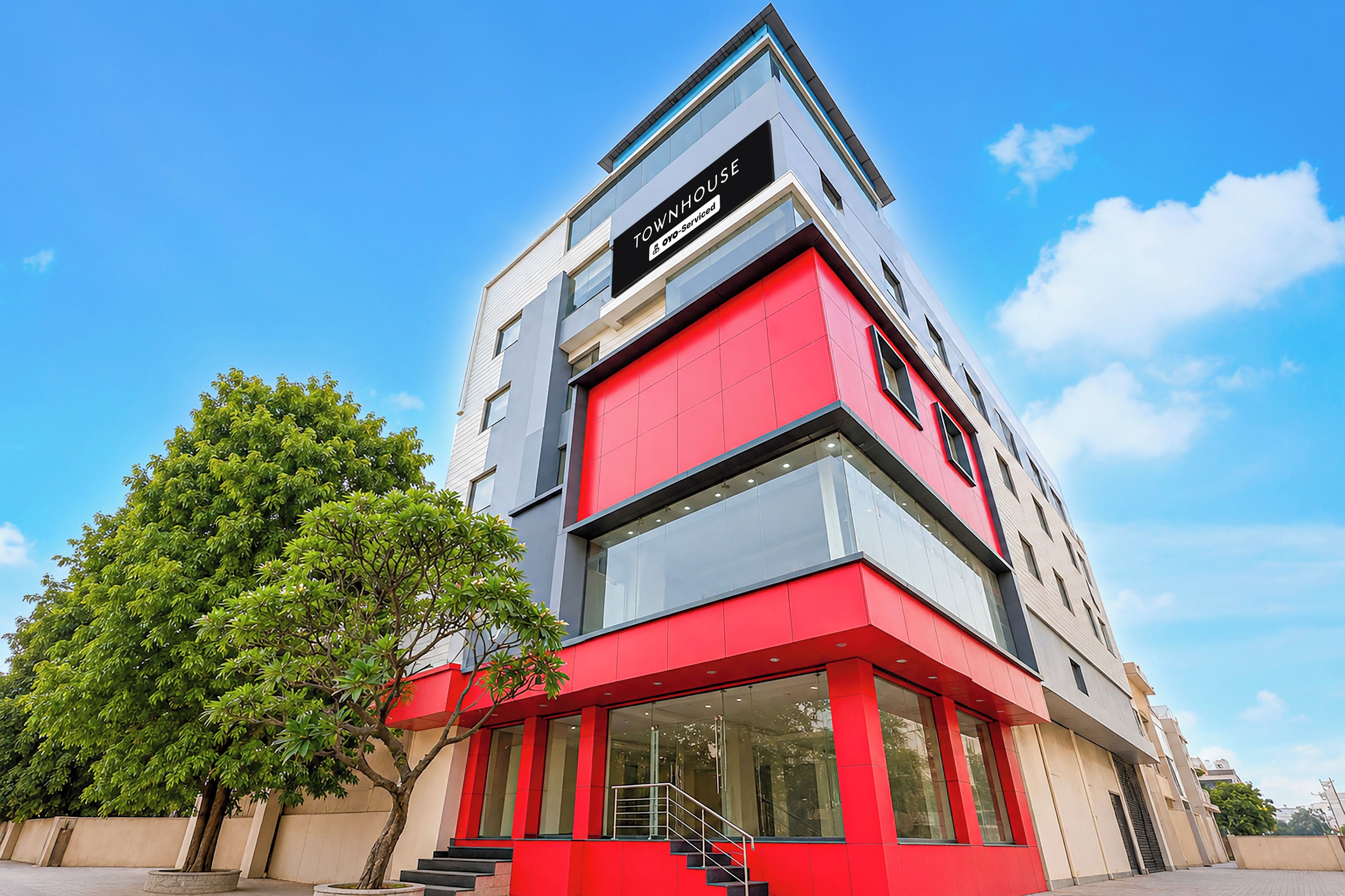 A modern building with a prominent red and grey facade, a visible staircase, and a clear sky.