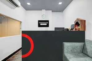 Uma área de recepção com um relógio, uma placa indicando serviço OYO e um pequeno santuário com objetos religiosos.
