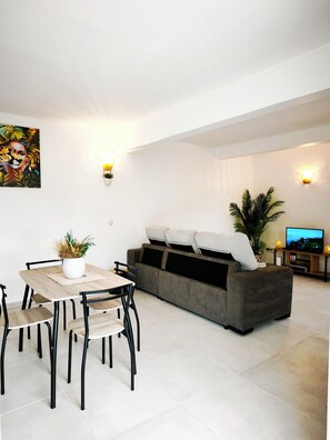 A modern living room with a sofa, TV, and dining area. - The Kaz'M T3 Family Home with a Barbecue and a Creole-Style Garden (Rivière-Pilote)
