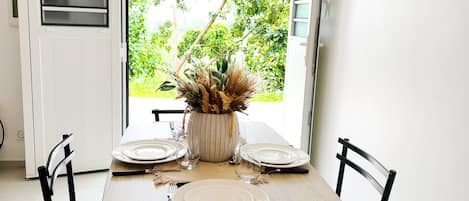 A dining area with a table set for four, chairs, a potted plant, and a wall-mounted light fixture.