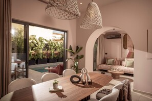 A modern interior with a dining area, a sofa, and a view of a pool and greenery outside. - Moncasa Segreta Collection (Agios Nikolaos)