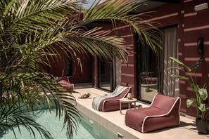 A poolside area with lounge chairs, a small table, and a potted plant. - Moncasa Segreta Collection (Agios Nikolaos)