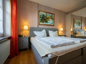 Ein Hotelzimmer mit einem großen Bett, zwei Nachttischen mit Lampen, einem Fenster mit rotem Vorhang und einem Gemälde an der Wand.
