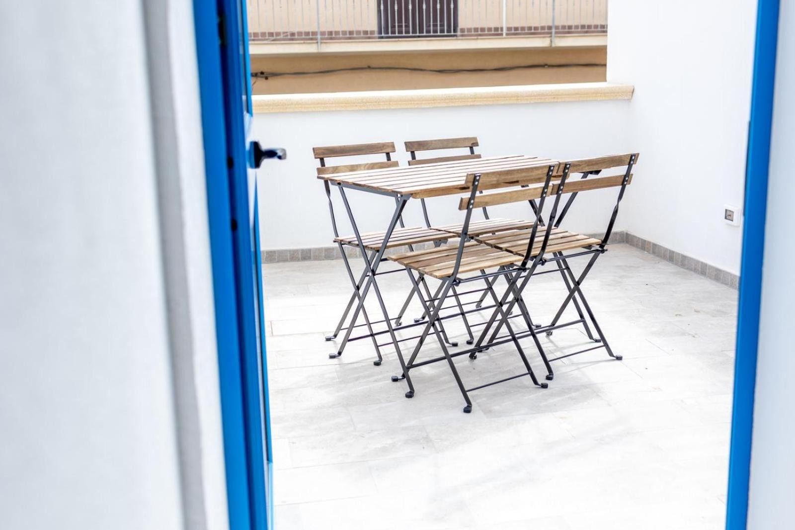 A room with a foldable table and chairs, a white wall, and a window with a view of a building.