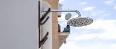 A balcony with a showerhead, a view of the sea, and a building in the background.