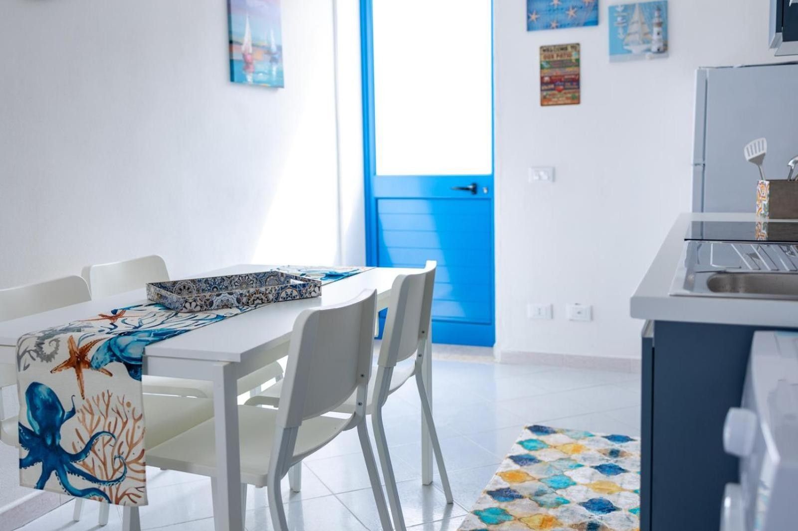 Een moderne keuken met witte kasten, een blauwe deur en een eetgedeelte met witte stoelen en een tafel.