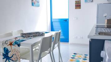Een moderne keuken met witte kasten, een blauwe deur en een eetgedeelte met witte stoelen en een tafel.