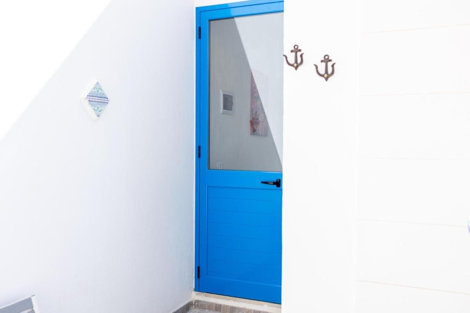 Een blauwe deur met een ruit, een klein decoratief object aan de muur en twee ankers.
