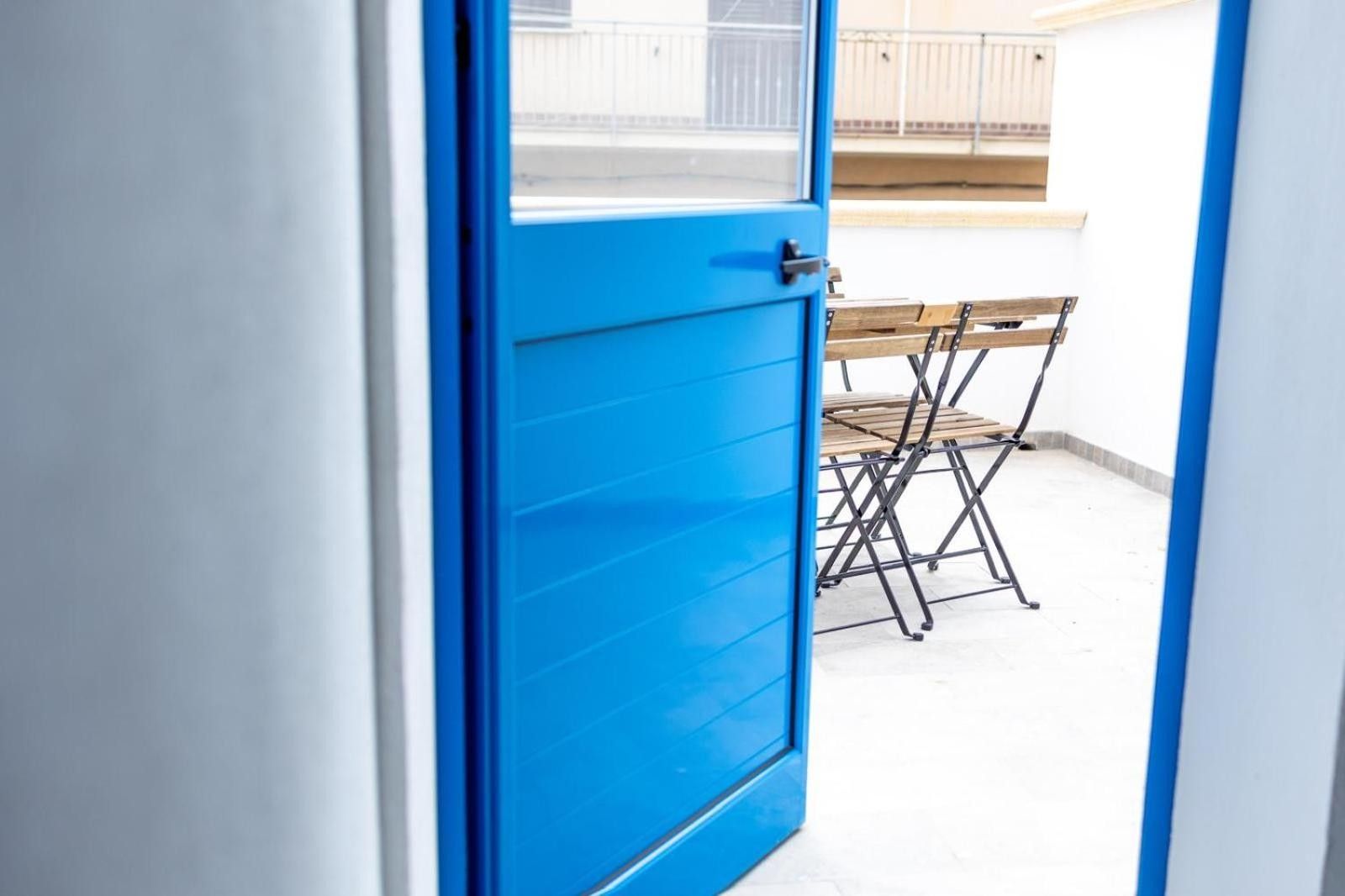 Une porte bleue qui donne sur un espace extérieur aménagé avec une table et des chaises en bois.