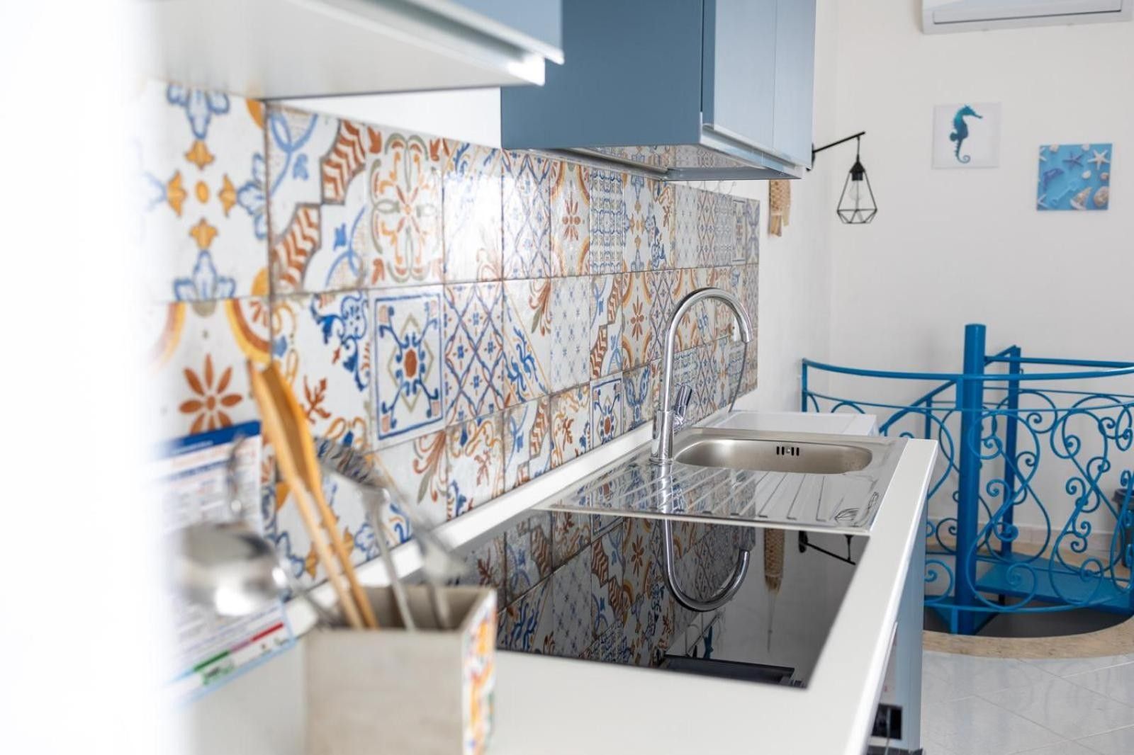 Une cuisine dotée d’un robinet moderne, d’un crédence à motifs et d’une rambarde métallique bleue.