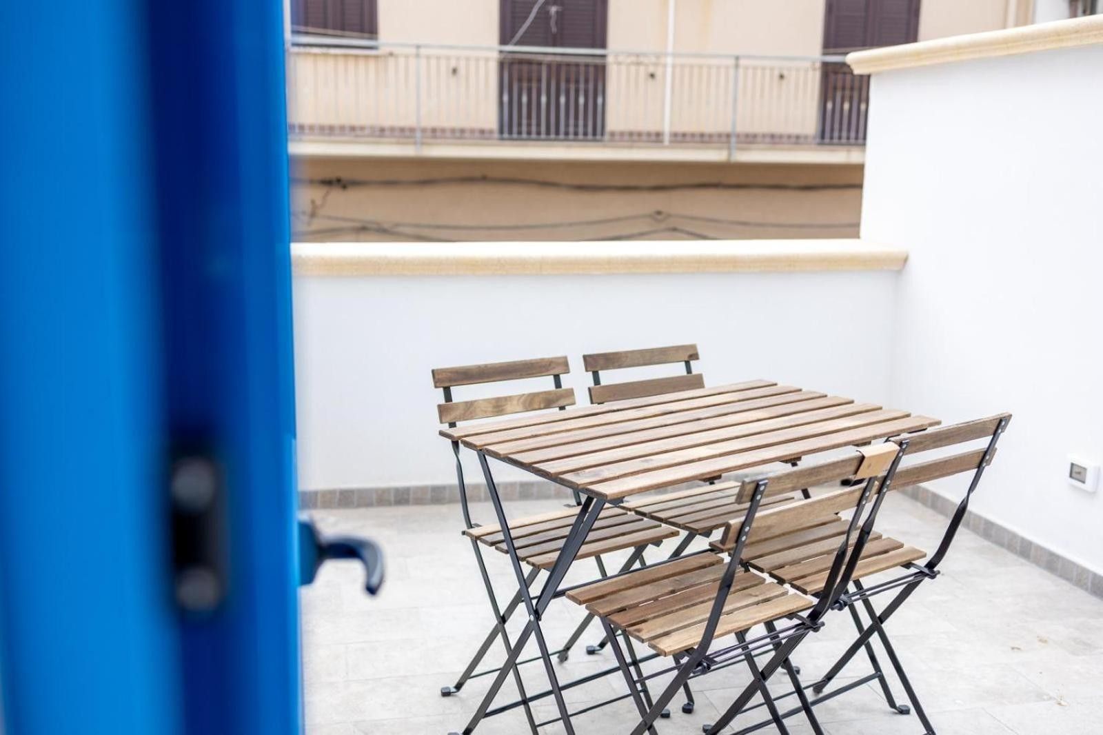 Een opklapbare houten tafel en stoelen staan op een balkon, met een witte muur en een hekwerk op de achtergrond.