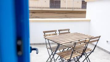 Een opklapbare houten tafel en stoelen staan op een balkon, met een witte muur en een hekwerk op de achtergrond.