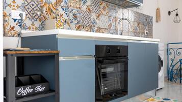 A compact kitchen with a built-in oven, a coffee bar, and a patterned backsplash.