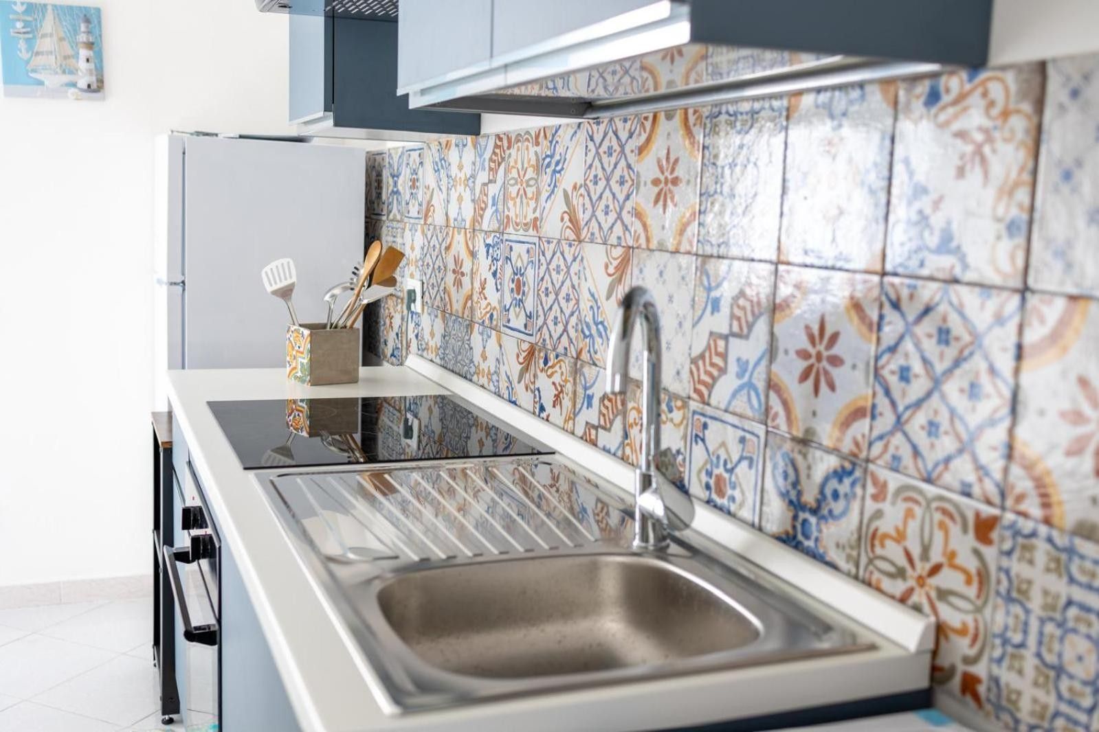 Una cucina con lavello in acciaio inossidabile, un rubinetto moderno e un piano di lavoro rivestito di piastrelle colorate.