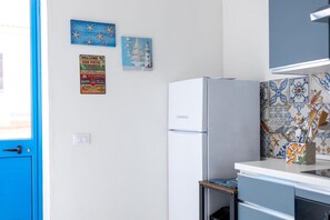 Cocina con refrigerador blanco, puerta azul y decoración de pared que incluye un faro y un letrero de bienvenida.