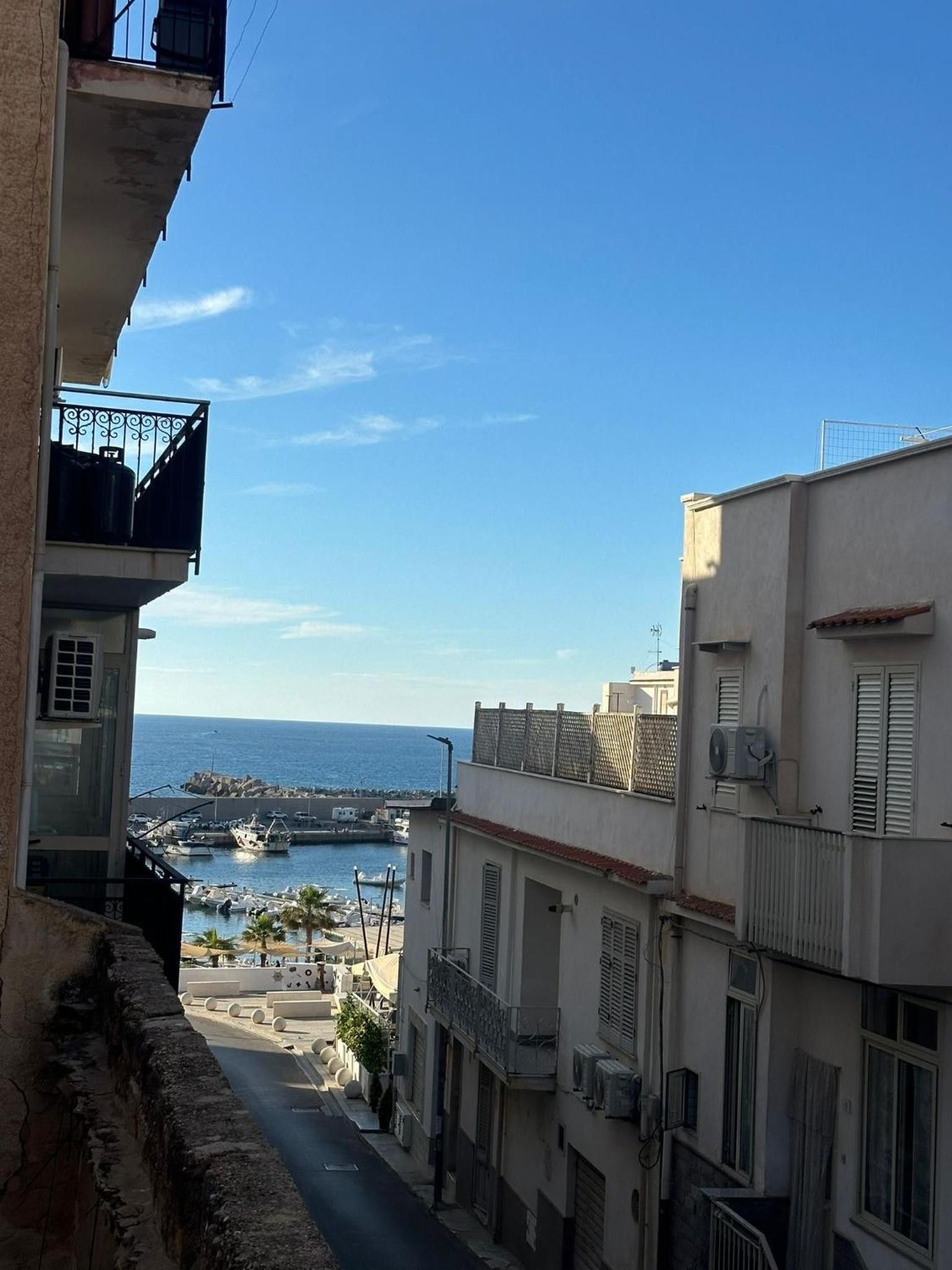 Una calle estrecha flanqueada por edificios, cielo despejado y una vista al mar y embarcaciones a lo lejos.