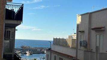 Una calle estrecha flanqueada por edificios, cielo despejado y una vista al mar y embarcaciones a lo lejos.