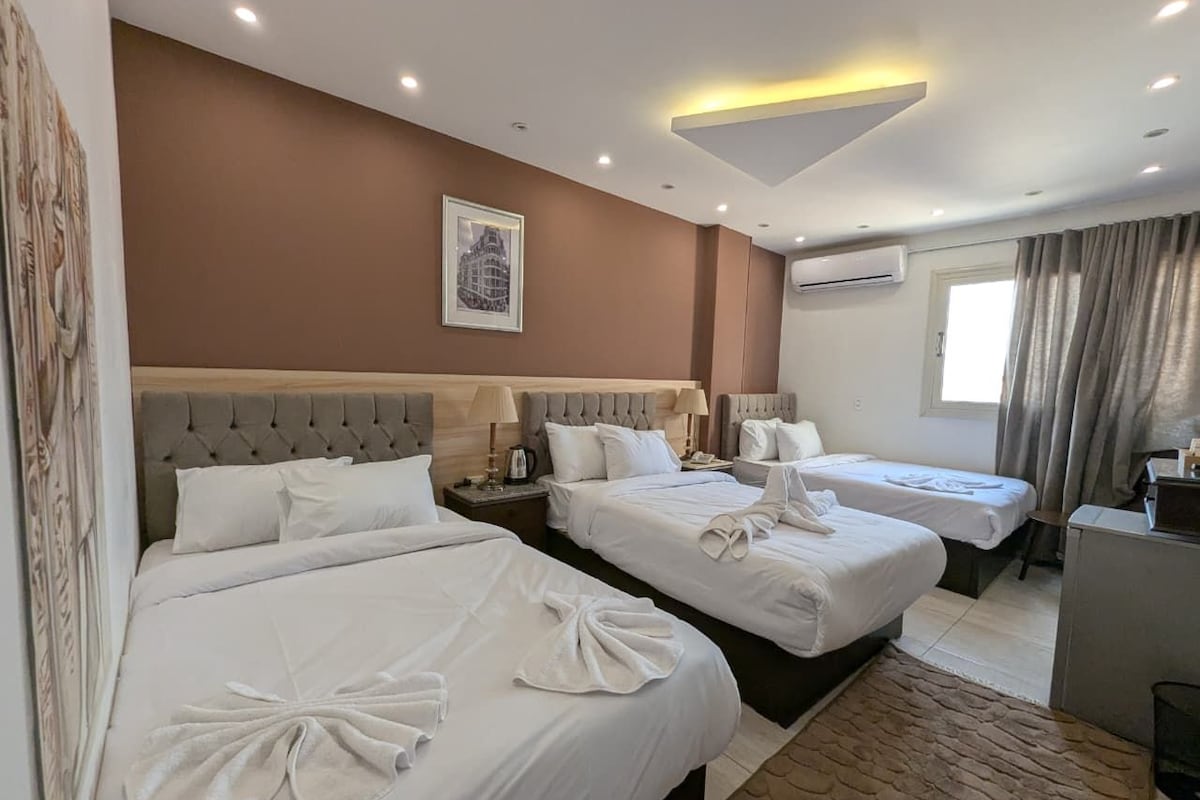 Habitación de hotel con tres camas, un escritorio y una ventana con cortinas.