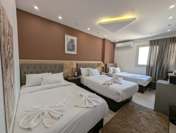 Habitación de hotel con tres camas, un escritorio y una ventana con cortinas.