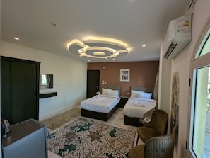 Habitación de hotel con dos camas, un escritorio, una silla, un tapete estampado y una lámpara en el techo.