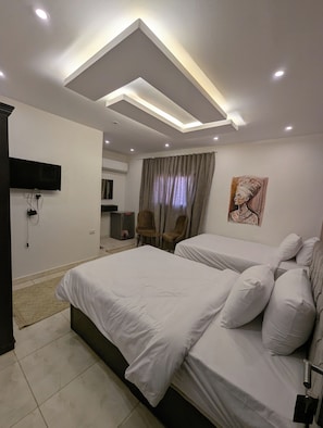 Ein Hotelzimmer mit zwei Betten, einem an der Wand befestigten Flachbildfernseher und einer Deckenleuchte.