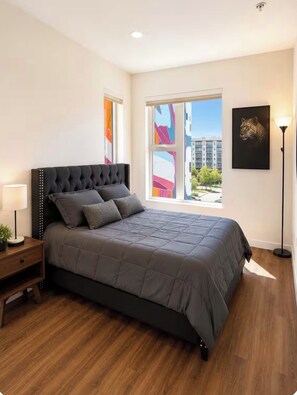 Ein Schlafzimmer mit einem großen Bett, einem Nachttisch, einer Stehlampe und einem Fenster mit Blick auf die Stadt.