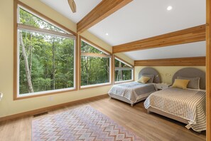 Ein Schlafzimmer mit zwei Betten, großen Fenstern und Blick auf Bäume.