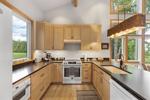 A modern kitchen with wooden cabinets, a built-in oven, and a large window providing a view of the outdoors. - New to the rental market. Perfect Getaway Chalet in Chinquapin (Glenville)