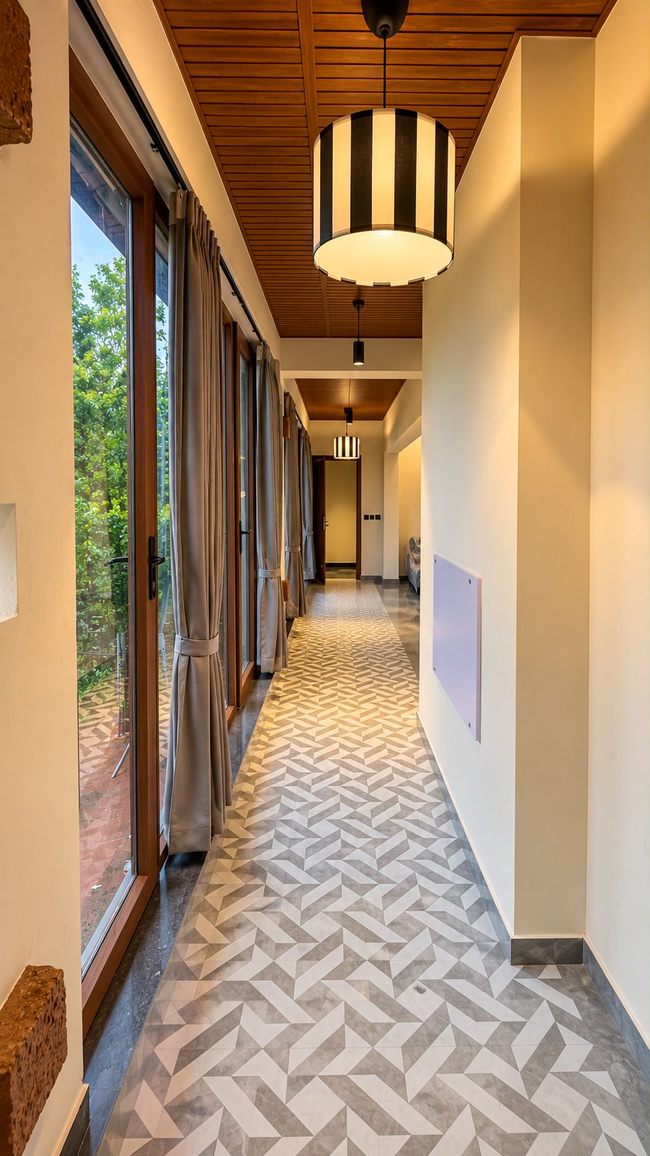 Un pasillo con piso de diseño geométrico, techo de vigas de madera y una lámpara colgante grande a rayas blanco y negro.
