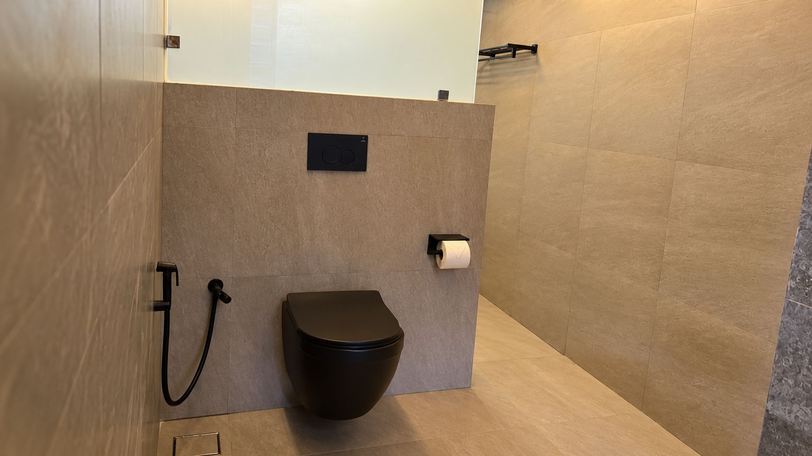 Casa de banho moderna com sanita, suporte de toalha e dispensador de papel.