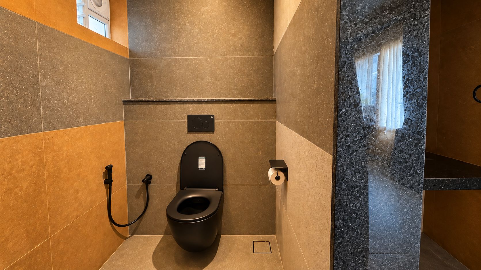 A modern bathroom with a black toilet, a hand dryer, and a paper towel dispenser.