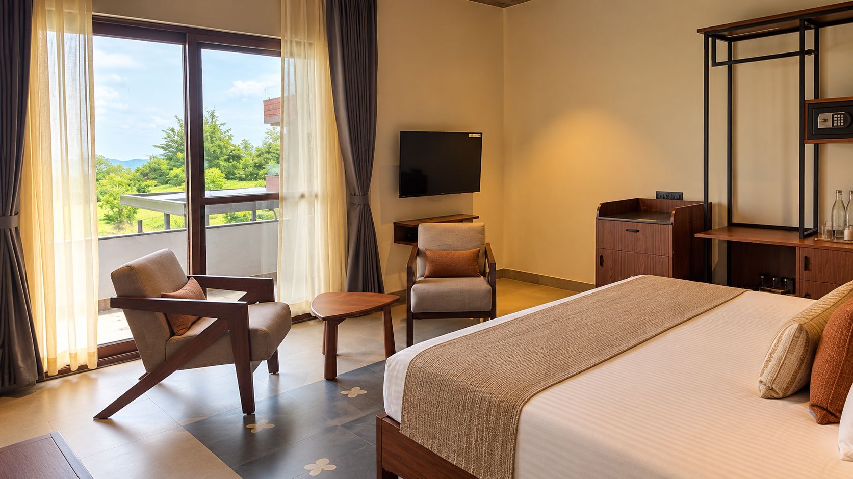 Quarto de hotel com cama, duas cadeiras, uma mesinha, televisão e escrivaninha com espelho.