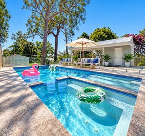 Ein Swimmingpool mit Liegebereich, überdachter Sitzgelegenheit und Blick auf Bäume und ein Haus.