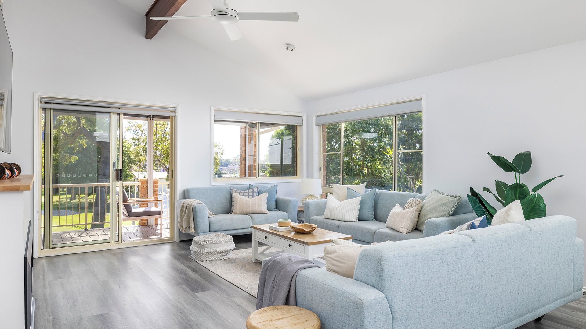 A spacious living room with a large sofa set, a coffee table, and a view of a garden through large windows.