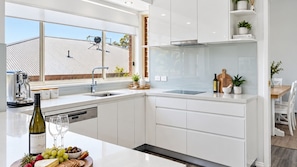 A modern kitchen with white cabinetry, a built-in oven, and a large window overlooking a rooftop. - Fairways at the Bay - Heated Pool and Green View (Nelson Bay)