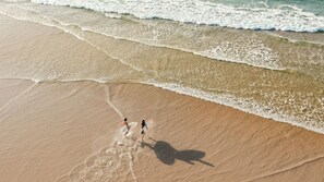 Eine Luftaufnahme eines Strandes, auf dem zwei Personen mit Surfbrettern entlanggehen.
