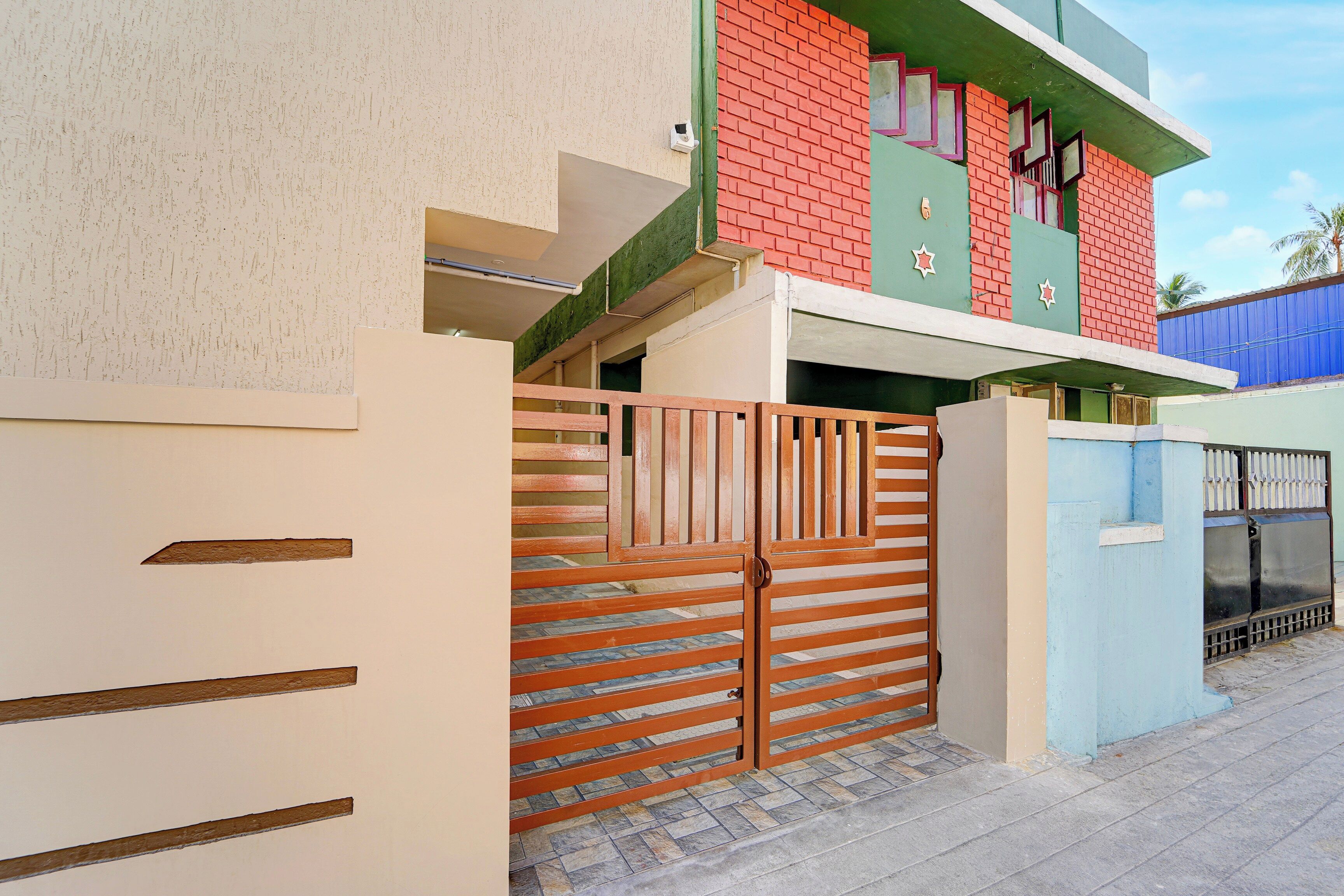 Un edificio residenziale con ingresso carrabile recintato, un portico piastrellato e una facciata blu e rossa.