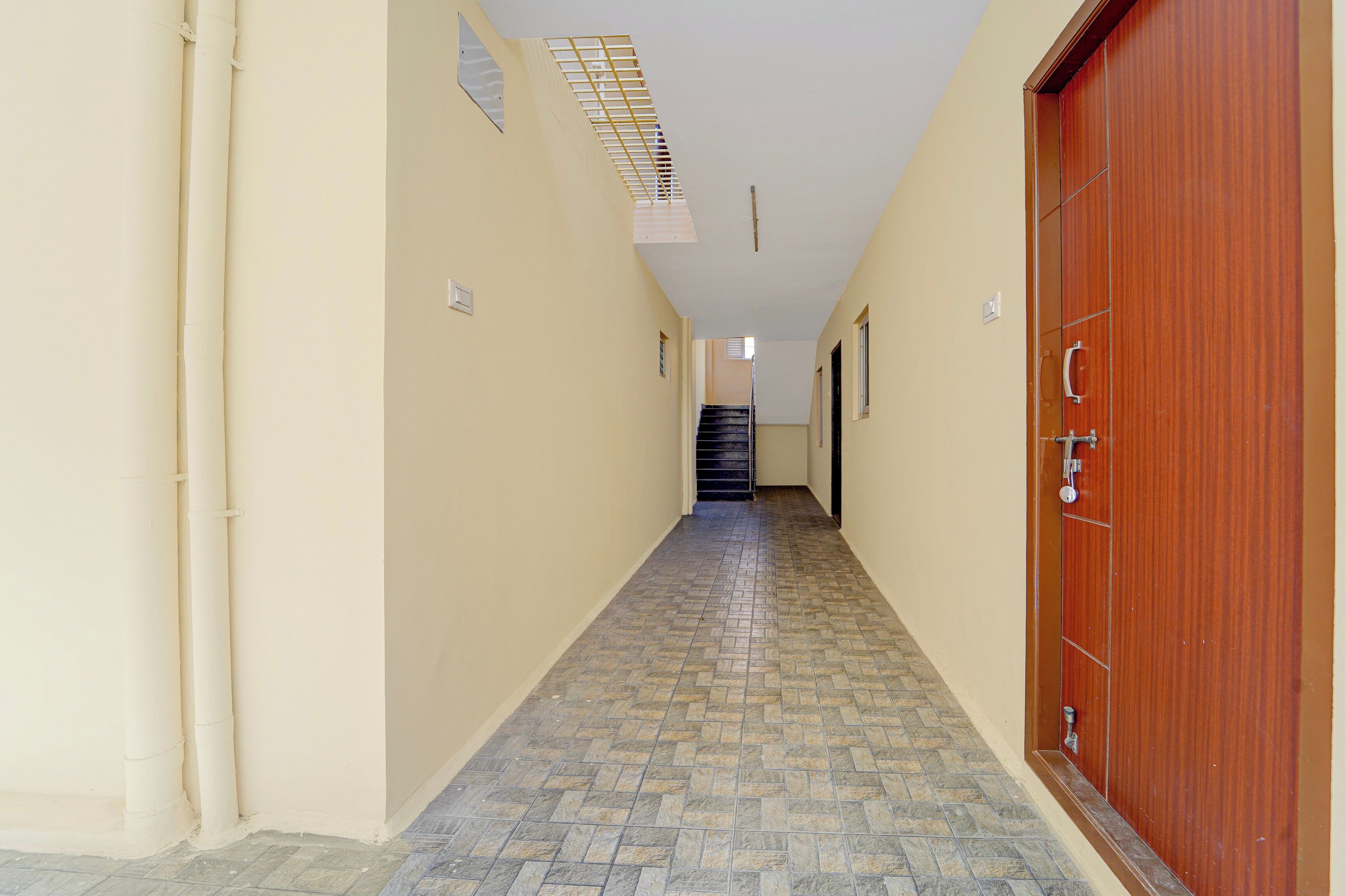 Un pasillo con suelo de baldosas, una puerta de madera a la derecha y una escalera al final.