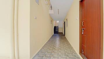 Un pasillo con suelo de baldosas, una puerta de madera a la derecha y una escalera al final.