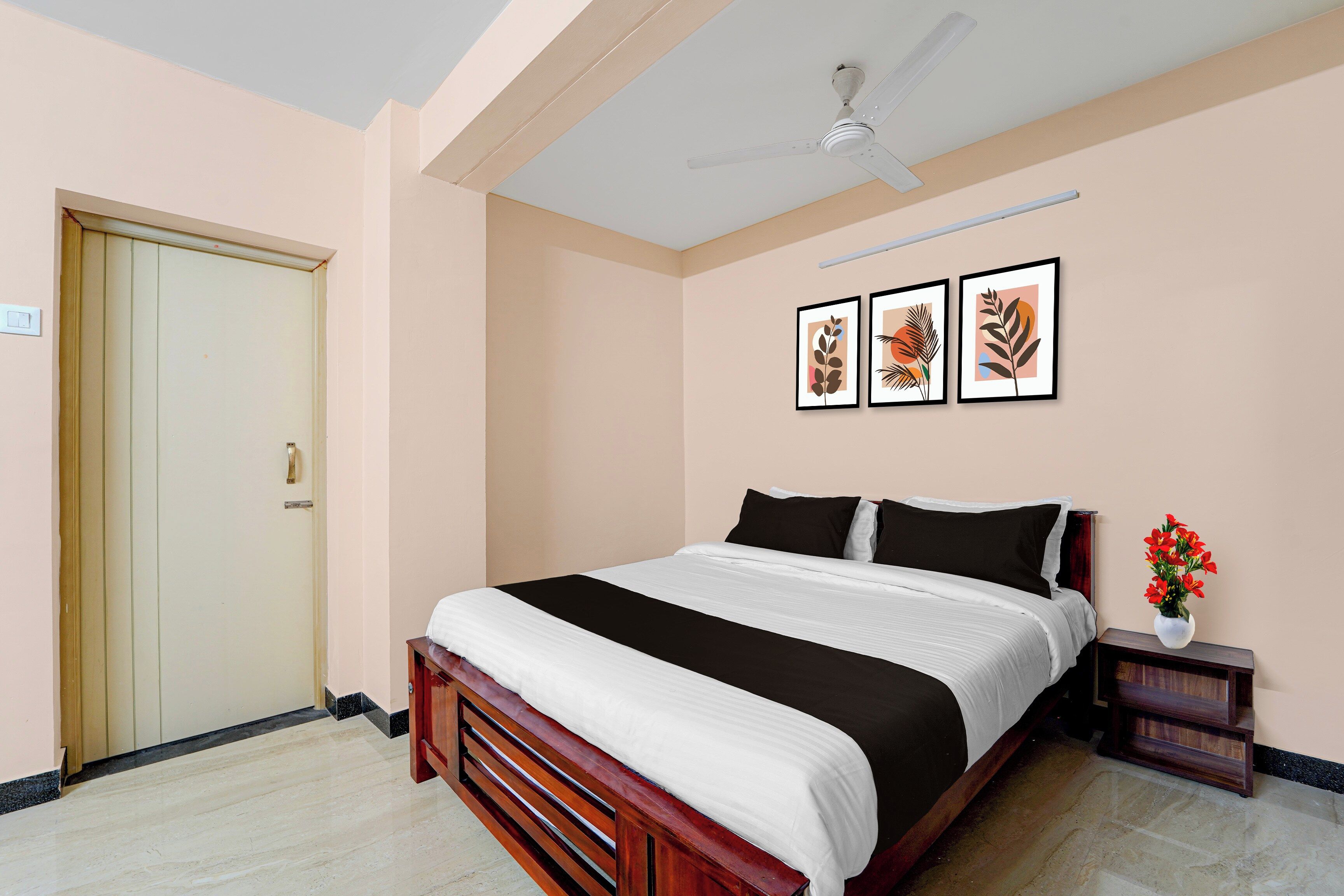 Un dormitorio con cama, ventilador de techo, una puerta y tres cuadros en la pared.