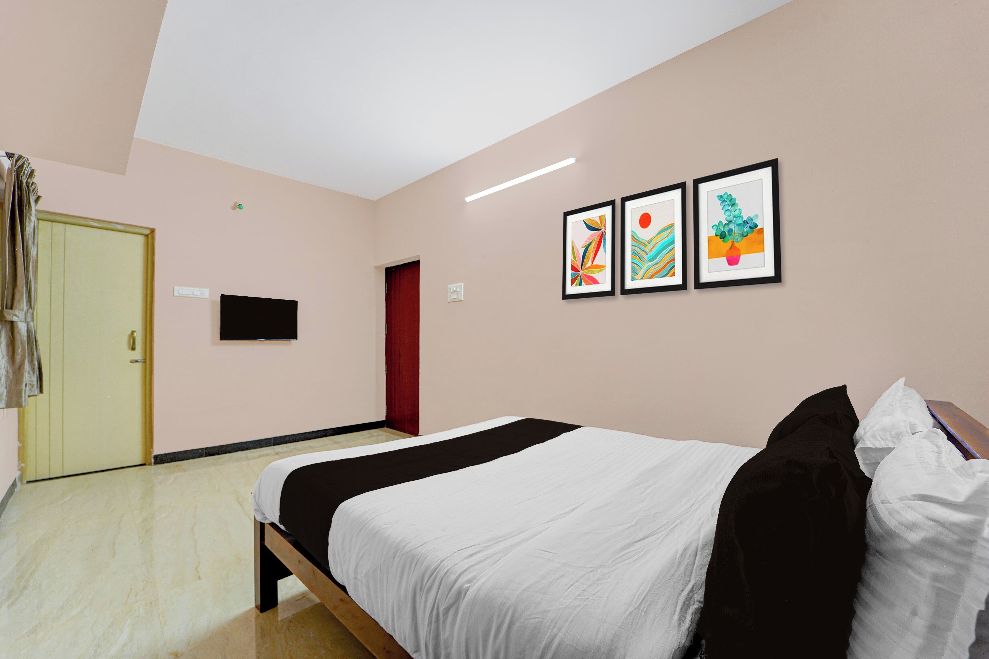 Quarto de hotel com uma cama, televisão de tela plana, uma porta e três obras de arte emolduradas na parede.