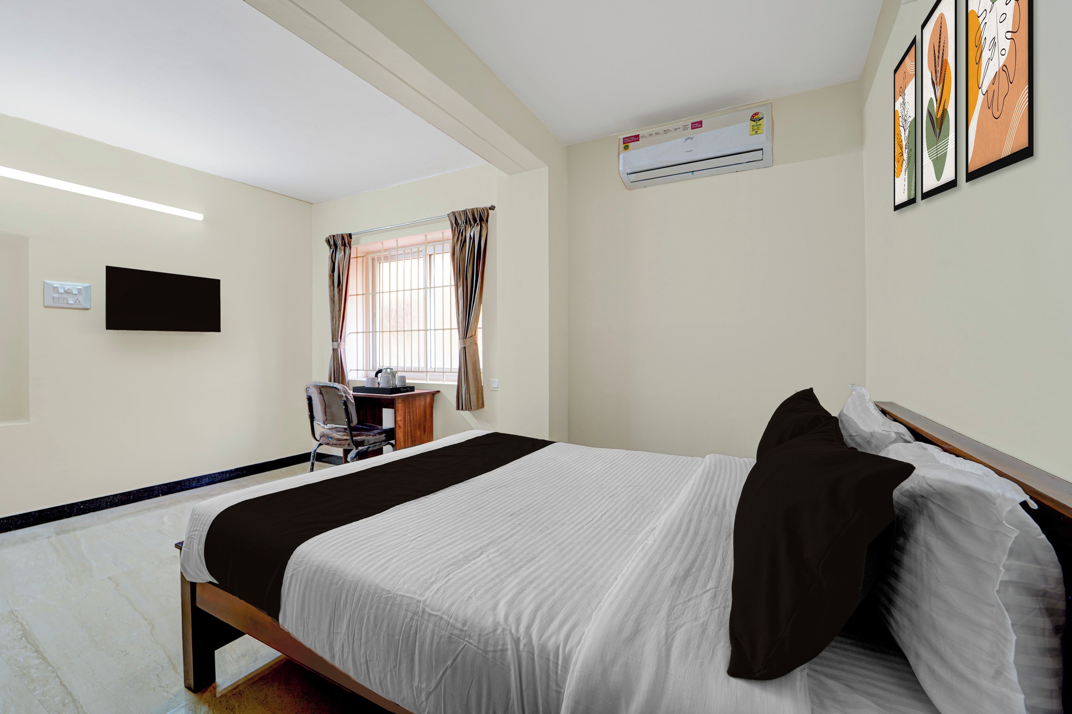 Una habitación de hotel con cama, escritorio, silla, televisión y aire acondicionado.