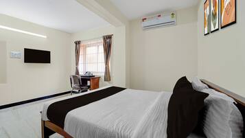 Una habitación de hotel con cama, escritorio, silla, televisión y aire acondicionado.